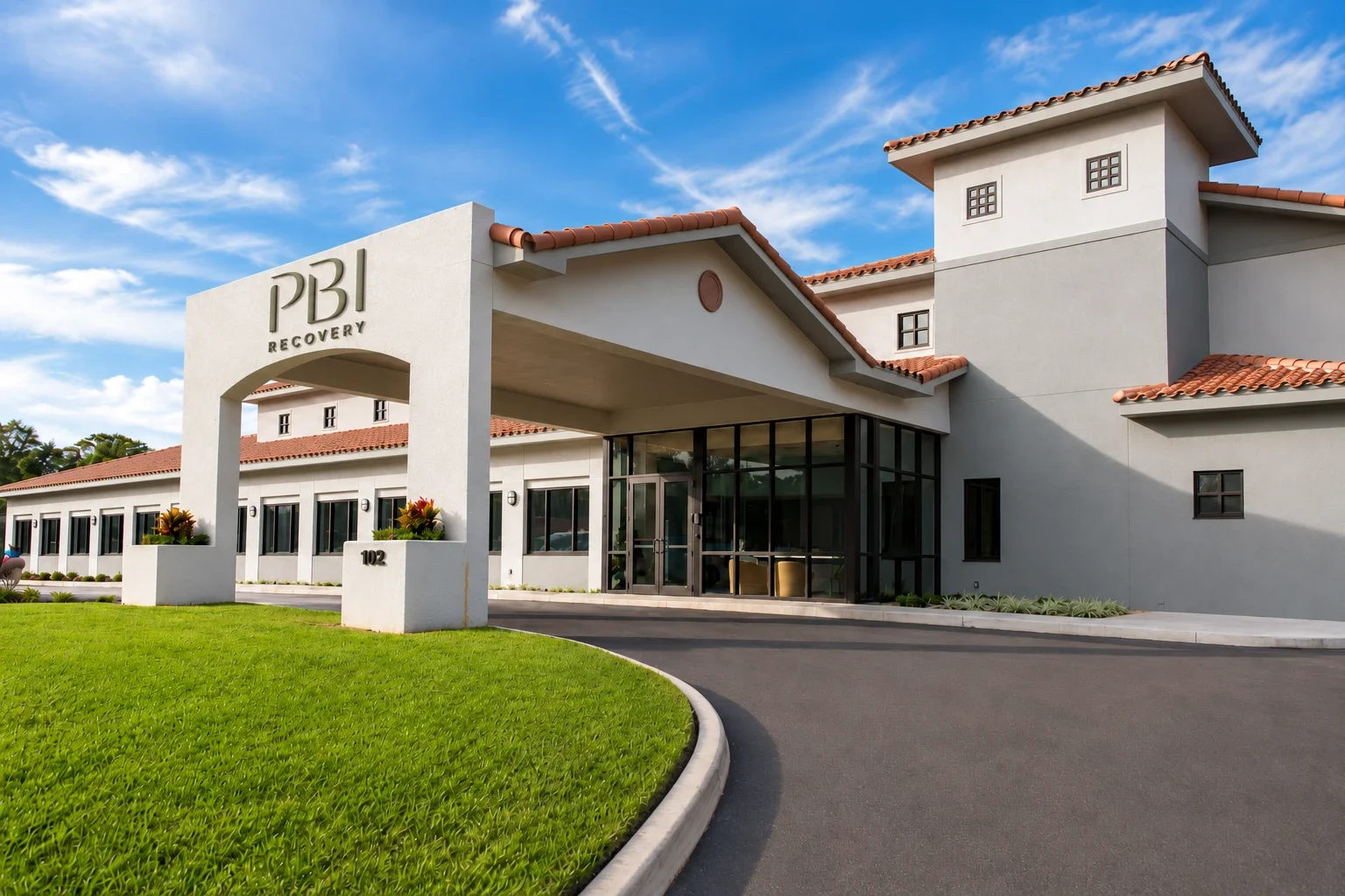 The front entrance of PBI Recovery, a white building with a red tile roof and a PBI Recovery archway